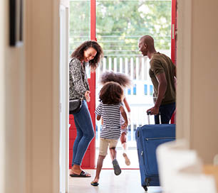 Family Standing By Front Door With Suitcase About To Leave For Vacation