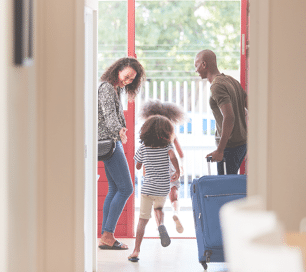 Family Standing By Front Door With Suitcase About To Leave For Vacation